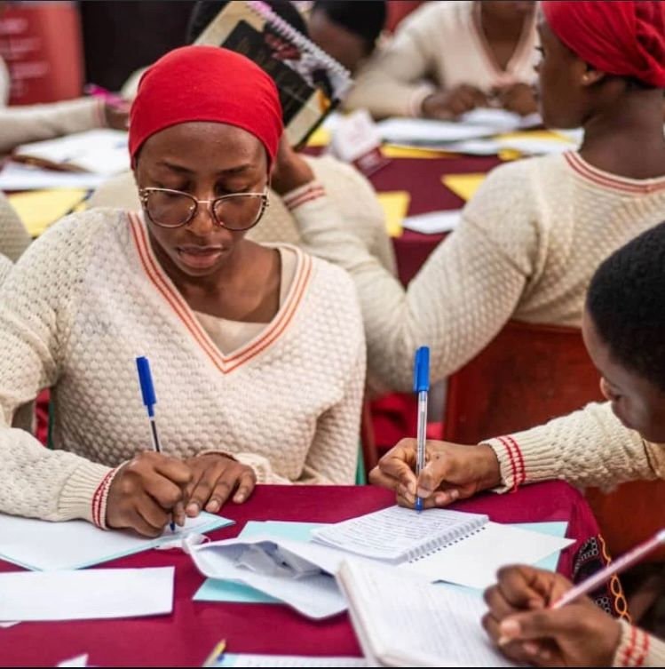 Lourdes students in their cream and red uniforms, writing at their desks
